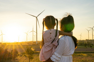 Mutter mit Kind auf dem Arm schauen auf Windräder im Sommer